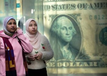 FILE - Egyptians walk past a poster depicting a U.S. dollar outside an exchange office in Cairo, Egypt, Thursday, Feb. 9, 2023. Egypt’s annual inflation rate set a record high in June, as the most populous Arab country continues to battle price hikes and a depreciating currency, the Egyptian statistics bureau said Monday, July 10, 2023. (AP Photo/Amr Nabil, File)