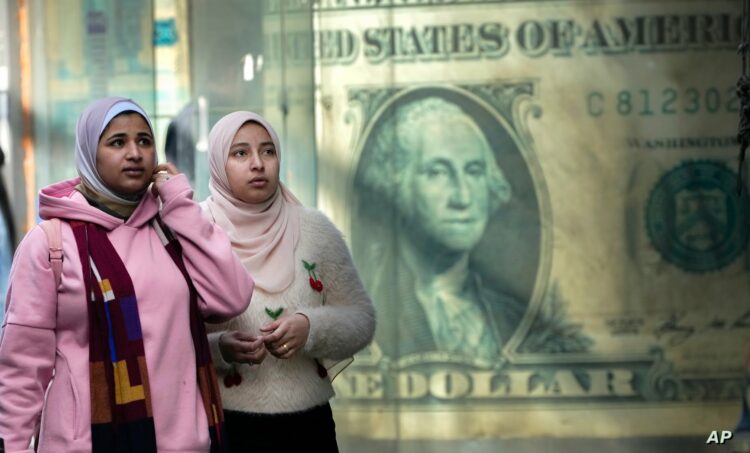 خبراء اقتصاد دوليون : انتظروا ارتفاع "قياسي" جديد للتضخم فى مصر 1 FILE - Egyptians walk past a poster depicting a U.S. dollar outside an exchange office in Cairo, Egypt, Thursday, Feb. 9, 2023. Egypt’s annual inflation rate set a record high in June, as the most populous Arab country continues to battle price hikes and a depreciating currency, the Egyptian statistics bureau said Monday, July 10, 2023. (AP Photo/Amr Nabil, File)