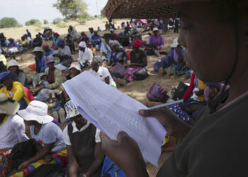 A woman reads out names of people waiting to receive food during a food distribution in Mangwe district southwestern Zimbabwe, amid a severe drought in Zimbabwe,Friday, March, 22, 2024. A new drought has left millions facing hunger in southern Africa as they experience the effects of extreme weather that scientists say is becoming more frequent and more damaging. (AP Photo/Tsvangirayi Mukwazhi)