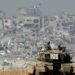 A picture taken from a position in southern Israel along the border with the Gaza Strip on January 19, 2024, shows an Israeli tank rolling along the fence as damaged buildings are see in the Gaza strip amid continuing battles between Israel and the militant group Hamas. (Photo by JACK GUEZ / AFP)