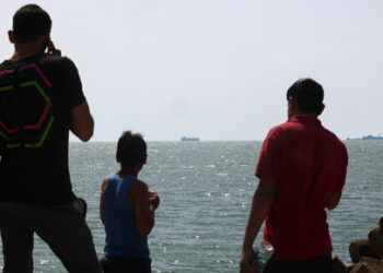 Palestinian youths stand on a jetty in Gaza City with a view of navy vessels off the coast as part of a humanitarian "maritime corridor" announced by US Central Command (CENTCOM) on May 17, 2024 amid the ongoing conflict in the Gaza Strip between Israel and Hamas. The US military said aid deliveries began on May 17 via a temporary pier in Gaza aimed at ramping up emergency humanitarian assistance to the war-ravaged Palestinian territory. (Photo by AFP)