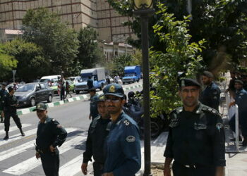 Police officers watch as a convoy carrying members of the British media leaves the British Embassy in Tehran, Iran August 23, 2015.  Britain reopened its embassy in Tehran on Sunday, nearly four years after protesters ransacked the ambassador's residence and burned the Union Jack. In a signal of the most striking thaw in Western ties with Iran for over a decade, Foreign Secretary Philip Hammond watched the British flag being raised in the garden of the opulent 19th century building while the national anthem played.   REUTERS/Darren Staples