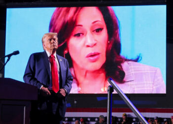 Republican presidential nominee and former U.S. President Donald Trump looks on as Democratic presidential nominee and U.S. Vice President Kamala Harris' face appears as a video plays on a screen, during a rally at Huntington Place in Detroit, Michigan, U.S. October 18, 2024.  REUTERS/Brian Snyder