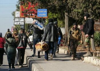 Anti-government fighters cross the path of residents carrying their belongings in Aleppo on November 30, 2024. Jihadists and their Turkish-backed allies breached Syria's second city of Aleppo on November 29, as they pressed a lightning offensive against forces of the Iranian- and Russian-backed government. (Photo by MUHAMMAD HAJ KADOUR / AFP)