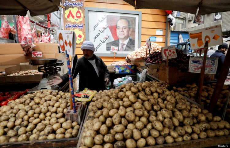 A vendor organizes his products besides a poster with an image of Egyptian President Abdel Fattah el-Sisi, at a vegetable market in Cairo, Egypt March 22, 2022. REUTERS/Mohamed Abd El Ghany